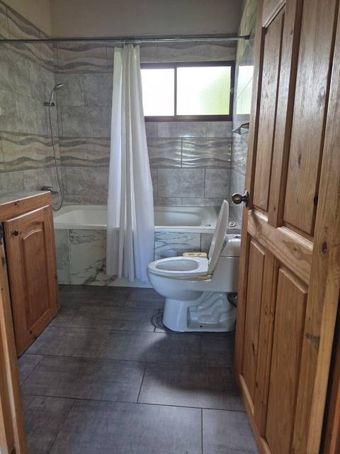 Baño con tina y cortina de ducha, acabados en tonos madera