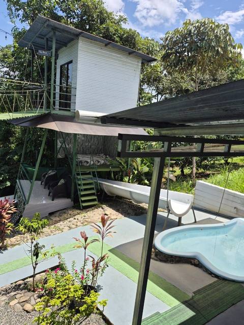 Cabaña elevada con tobogán hacia la piscina y el puente de canopy de fondo